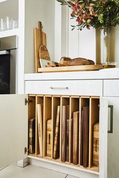 a kitchen cabinet filled with lots of wooden utensils and cutting boards next to a potted plant