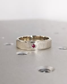 a close up of a wedding ring with a red stone in it on a silver surface