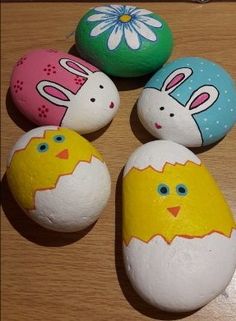 four painted rocks with easter eggs in the shape of rabbits and chickens on them, sitting on a wooden surface