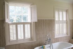 a bath tub sitting next to two windows with shutters on the side of it