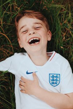 a young boy laying in the grass with his mouth open