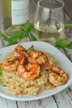 a white plate topped with rice and shrimp next to a bottle of wine