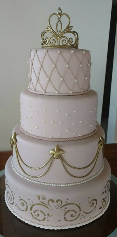 a three tiered pink and gold wedding cake with pearls on the top, sitting on a table