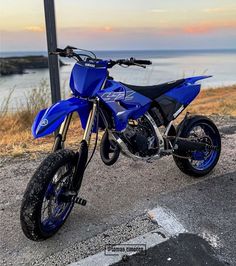 a blue dirt bike parked on top of a parking lot next to the ocean at sunset