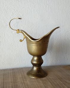 a brass vase with a hook in the middle sitting on a wooden table next to a white wall