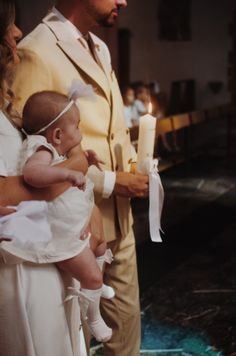 a man in a suit holding a baby while standing next to a woman wearing a white dress