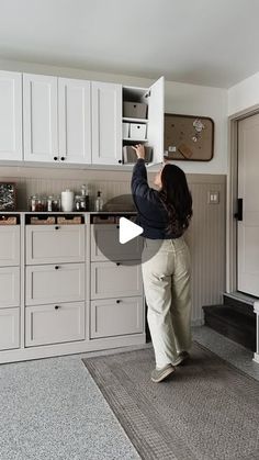 a woman standing in front of a kitchen counter with drawers and cupboards on the wall