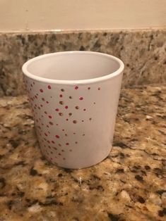 a white cup sitting on top of a counter next to a marble countertop covered in red dots