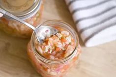 a person holding a spoon in a jar filled with food on a wooden table next to a towel