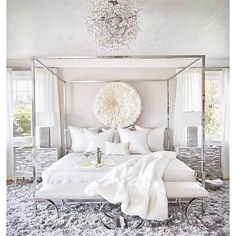 a white bedroom with a canopy bed and chandelier hanging from it's ceiling