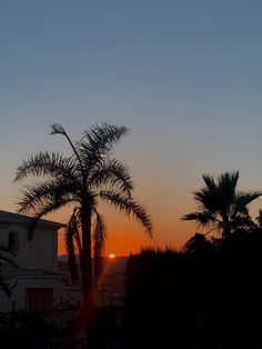 the sun is setting behind two palm trees in front of a house and some buildings