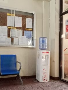 a blue bench sitting next to a water cooler in front of a wall with papers on it