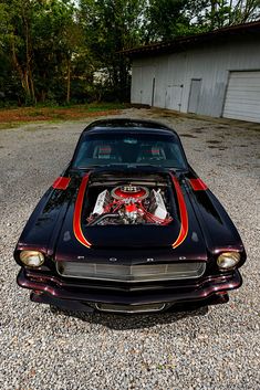 an old muscle car parked on gravel with its hood up and the engine in it's trunk