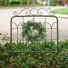 a green metal frame with a wreath on it in the middle of some grass and bushes