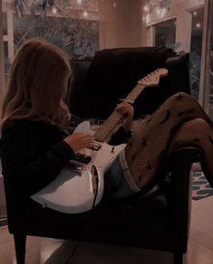 a woman sitting in a chair playing an electric guitar