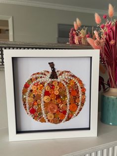 there is a framed picture with buttons in the shape of a pumpkin on top of a shelf