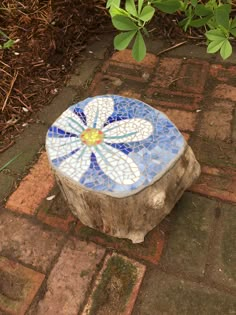 a small blue and white flower sitting on top of a tree stump next to a bush