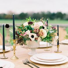 the table is set with white plates and silverware, black candles, and an arrangement of flowers