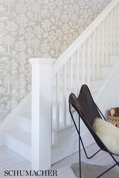 a chair sitting in front of a stair case next to a wallpapered staircase