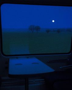 the view from inside a vehicle looking out at a field with trees and a full moon