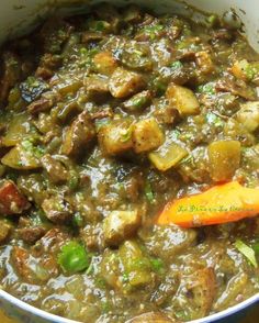 a bowl filled with meat and vegetables on top of a colorful table cloth next to a wooden spoon