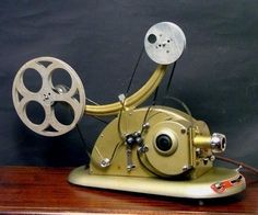 an old fashioned movie projector sitting on top of a wooden table next to a black wall