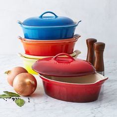 various colored pots and pans on a white table with garlic, pepper, and onion