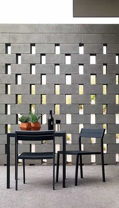 two chairs and a table in front of a brick wall with cactuses on it