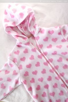 a baby's pink and white outfit with hearts on the hood is laying on a bed