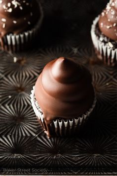 three chocolate cupcakes are sitting on a black tray with white sprinkles