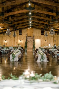 the inside of a barn with tables and chandeliers on each side of the room