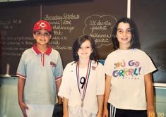 three children standing in front of a chalkboard with medals around their necks and numbers on it