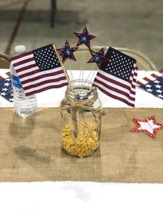 a jar filled with popcorn sitting on top of a table next to an american flag