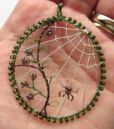 a hand holding a wire and bead spider web ornament in it's palm