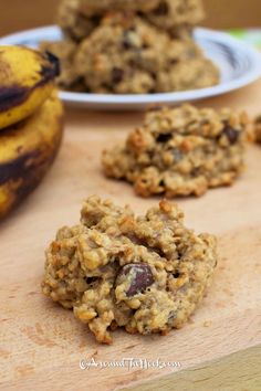 three cookies and two bananas on a wooden cutting board next to some other food items