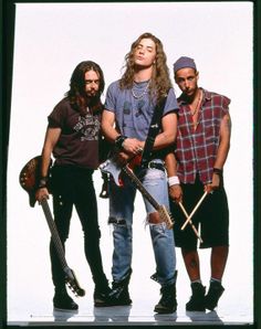 three young men standing next to each other with guitars and drums in their hands, all looking up