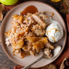 an apple crisp with ice cream and caramel sauce on a plate next to apples