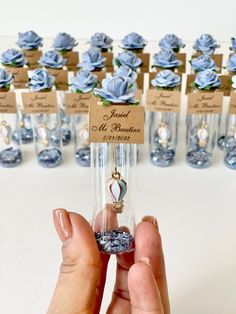 a person holding up a tiny glass bottle with blue flowers in it and small tags attached to the bottles