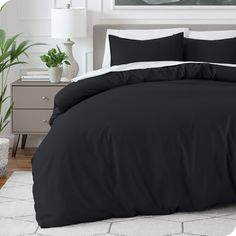 a bed with black sheets and pillows in a room next to a potted plant