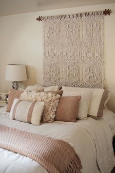 a white bed topped with lots of pillows next to a wall mounted headboard and lamp