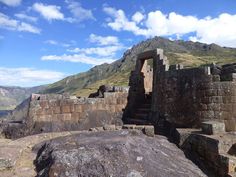 an old stone structure on the side of a mountain with mountains in the background and clouds in the sky