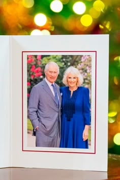 an old man and woman are standing next to each other in front of a christmas tree