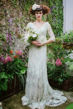 a woman standing in front of flowers wearing a dress with long sleeves and a flower crown on her head