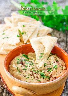 a bowl filled with hummus and chips on top of a wooden cutting board next to some tortilla chips