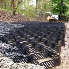 many black plastic containers are stacked on top of each other in the dirt near some trees