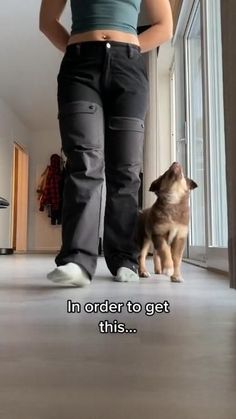 a woman standing next to a dog on top of a hard wood floor in front of a window