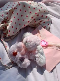 two stuffed animals laying on top of a bed next to a pink envelope with hearts