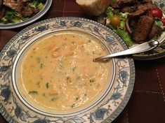 there is a bowl of soup on the table next to some meat and salads