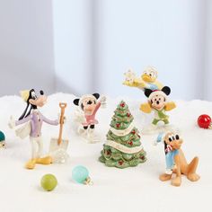 a group of mickey mouse figurines standing around a christmas tree