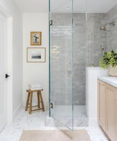 a bathroom with a walk in shower next to a white counter top and wooden stool